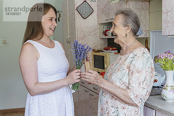 Lächelnde Frau schenkt der Großmutter zu Hause einen Strauß Lavendelblüten und ein Geschenk