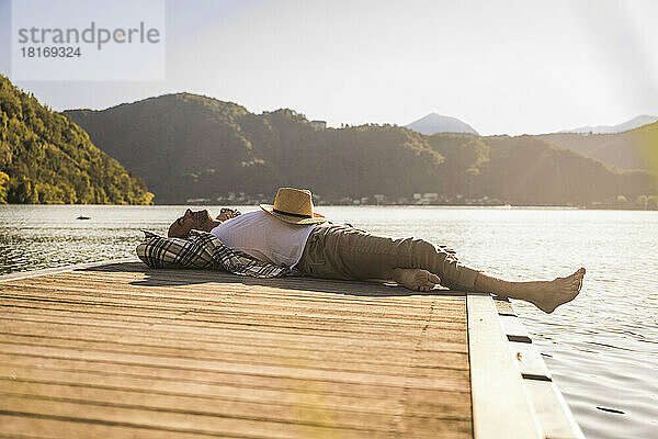 Man with hat resting on jetty over lake