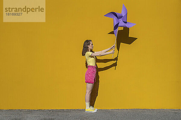 Frau mit Windradspielzeug steht vor leuchtend gelber Wand