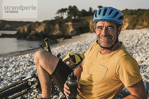 Glücklicher Mann mit Fahrradhelm entspannt sich am Strand