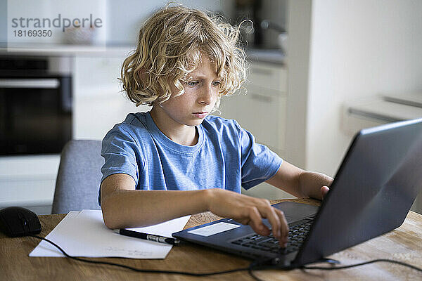 Junge mit blonden Haaren benutzt Laptop auf Tisch zu Hause