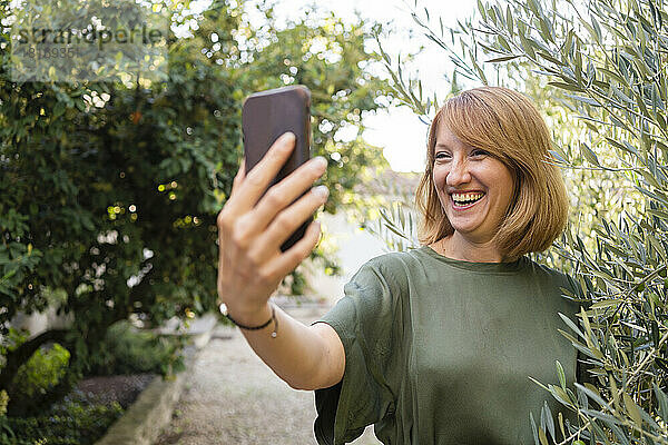 Glückliche reife Frau  die im Garten ein Selfie mit dem Smartphone macht