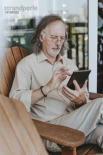 Älterer Mann sitzt auf Stuhl und benutzt Tablet-PC auf der heimischen Terrasse