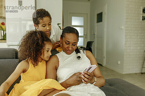 Frau teilt Smartphone mit Kindern auf Sofa zu Hause