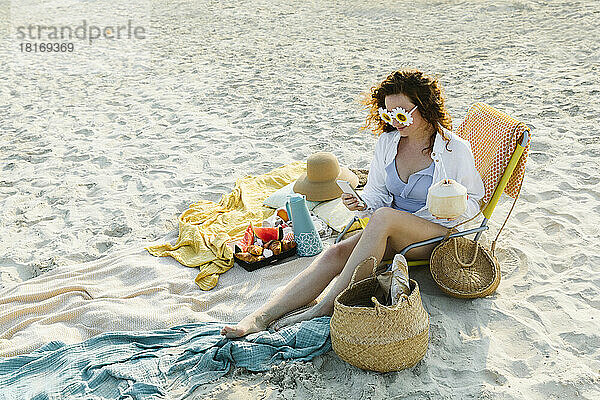 Lächelnde Frau mit Blumensonnenbrille und Smartphone am Strand