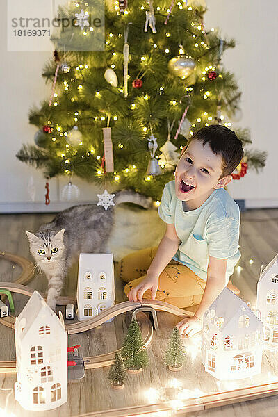 Fröhlicher Junge mit Katze  der zu Hause in der Nähe des Weihnachtsbaums spielt