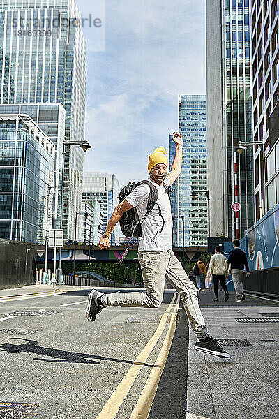 Mann mit Strickmütze springt auf Straße vor Gebäuden