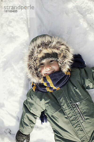 Lächelnder Junge  der auf Schnee liegt