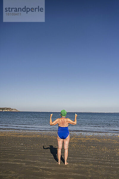 Frau schaut an einem sonnigen Tag aufs Meer und lässt Muskeln spielen