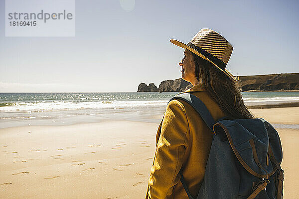 Frau mit Rucksack steht an einem sonnigen Tag am Strand