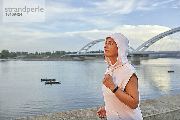 Frau trägt Kapuzenshirt beim Joggen am Fluss