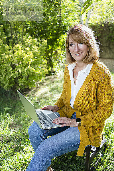 Lächelnder Freiberufler sitzt mit Laptop im Garten