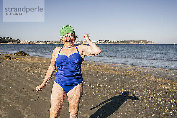 Glückliche ältere Frau  die am Strand Muskeln spielen lässt
