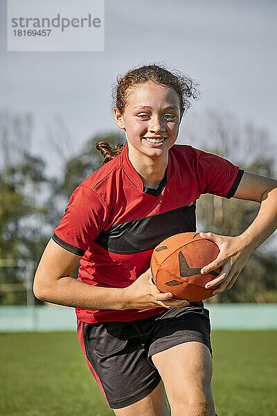 Glückliches Mädchen mit Rugbyball beim Üben an einem sonnigen Tag