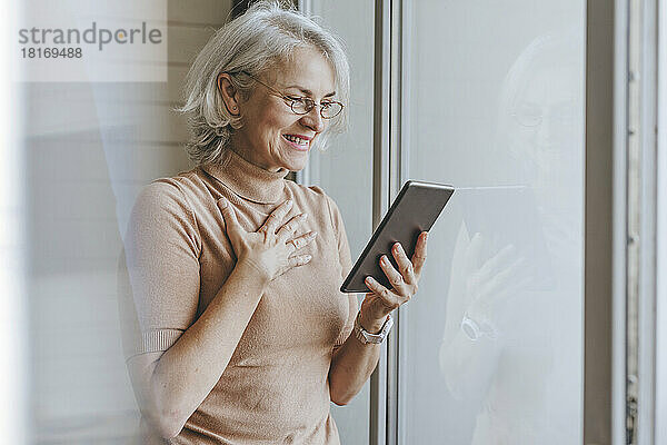 Happy mature woman on video call through tablet PC at home