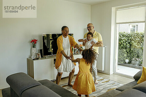 Glückliche Kinder mit Eltern  die zu Hause im Wohnzimmer tanzen