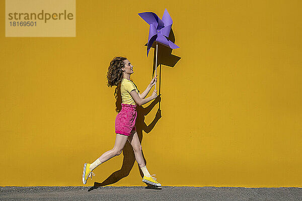 Frau läuft mit Windradspielzeug vor gelber Wand