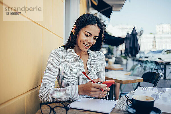 Glückliche Geschäftsfrau benutzt Smartphone im Straßencafé
