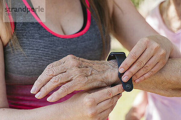 Fitnesstrainer justiert Smartwatch an der Hand einer älteren Frau
