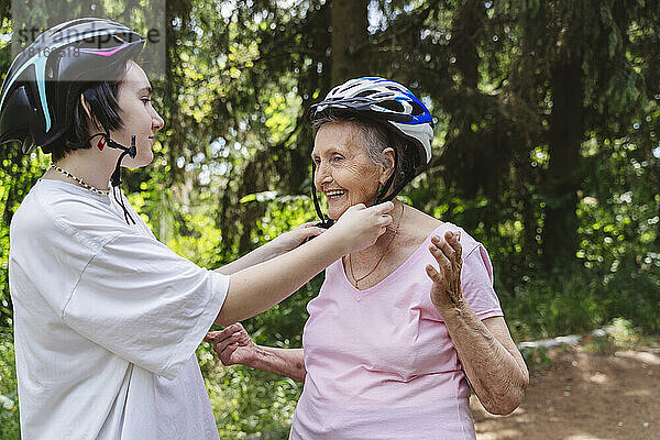 Mädchen hilft Urgroßmutter mit Fahrradhelm im Park