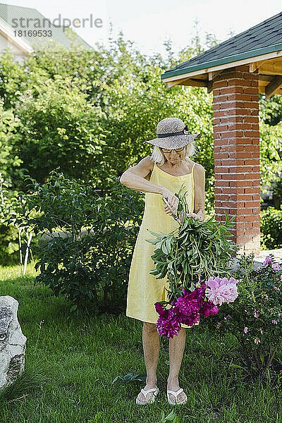 Ältere Frau schneidet Blätter und hält einen Blumenstrauß im Garten