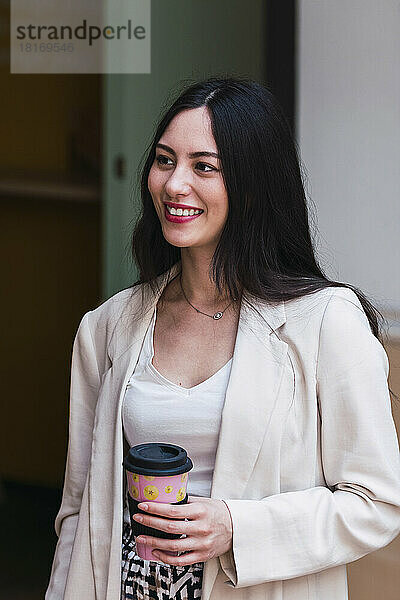 Lächelnde Geschäftsfrau hält Einwegkaffeetasse im Büro