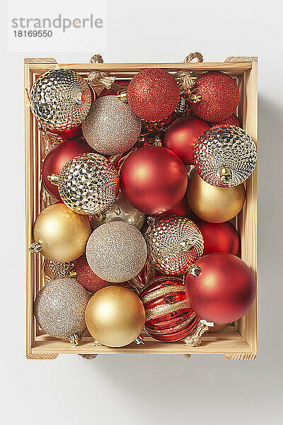 Wooden box with shiny christmas baubles against white background