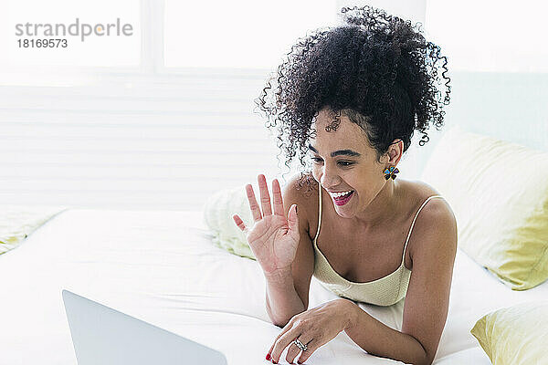 Happy woman waving on video call through laptop at home