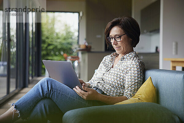 Frau sitzt zu Hause auf dem Sofa und benutzt Laptop