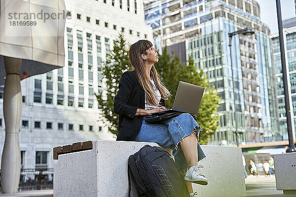 Freiberufler mit Laptop sitzt auf einem Sitzplatz vor Gebäuden