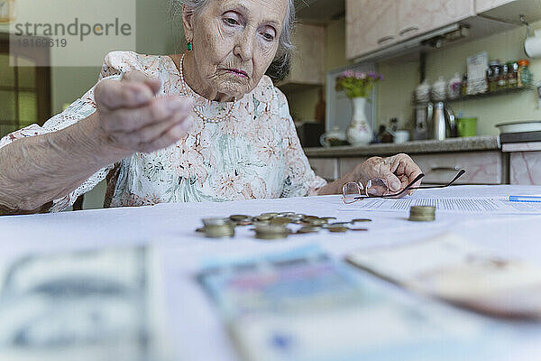 Verwirrte Seniorin blickt zu Hause auf Ersparnisse auf dem Tisch