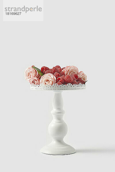 Himbeeren mit Rosen auf einem Kuchenständer vor weißem Hintergrund