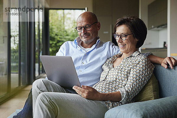 Glückliche ältere Frau mit Mann  der zu Hause Laptop benutzt