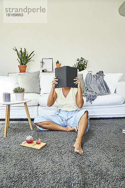 Frau bedeckt Gesicht mit Tagebuch vor Sofa zu Hause