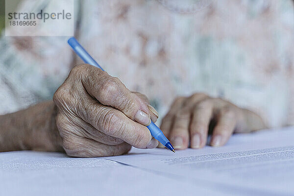 Faltige Hand einer älteren Frau  die zu Hause Vertragspapiere unterzeichnet