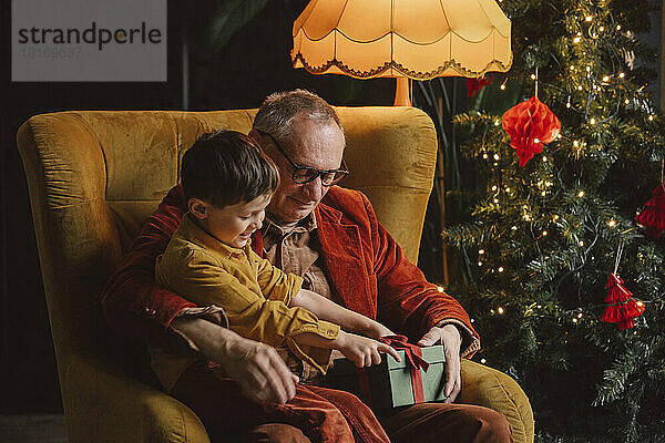 Glücklicher Enkel und Großvater sitzen mit Geschenkbox zu Hause
