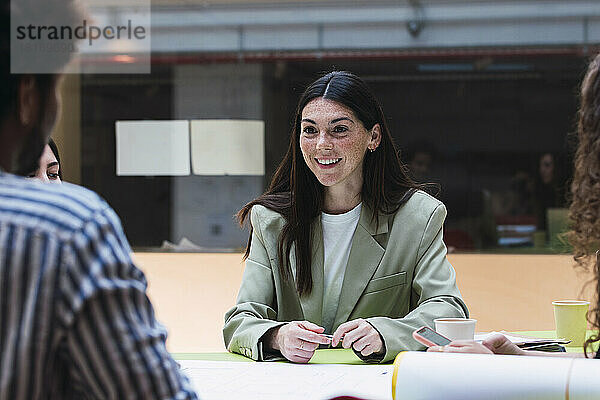 Lächelnde Geschäftsfrau blickt Kollegen im Büro an