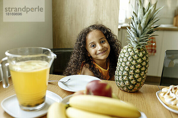 Lächelndes Mädchen mit Ananas auf dem Esstisch zu Hause