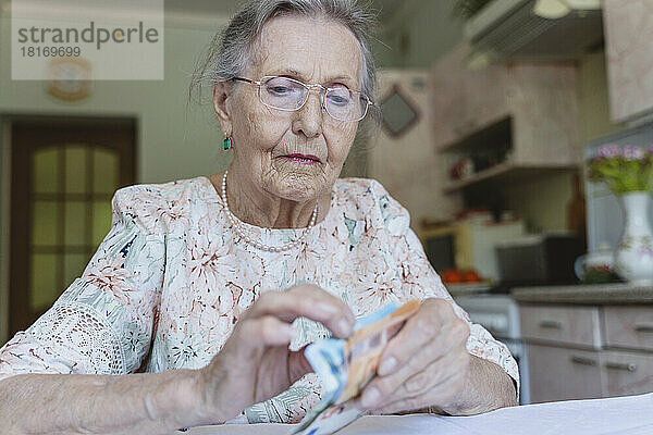 Senior woman with eyeglasses counting paper currency at home