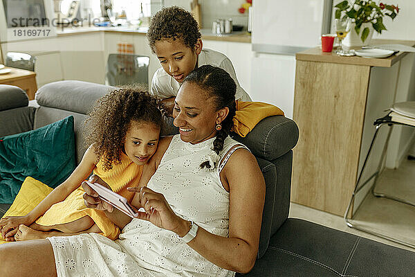 Glückliche Frau teilt Smartphone mit Tochter und Sohn auf dem heimischen Sofa