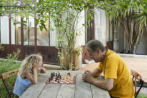 Enkelin und Großvater spielen Schach im Garten