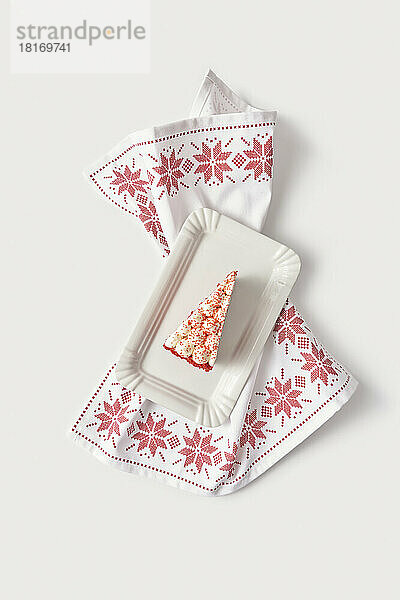 Slice of red velvet cake in white tray on embroidered table napkin against white background