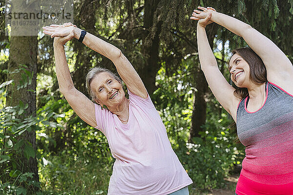 Fröhlicher Fitnesstrainer mit Seniorin beim Dehntraining im Park