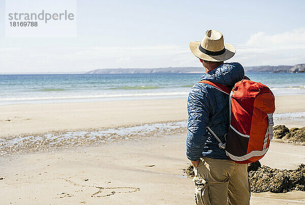 Mann mit Rucksack bewundert das Meer am Strand