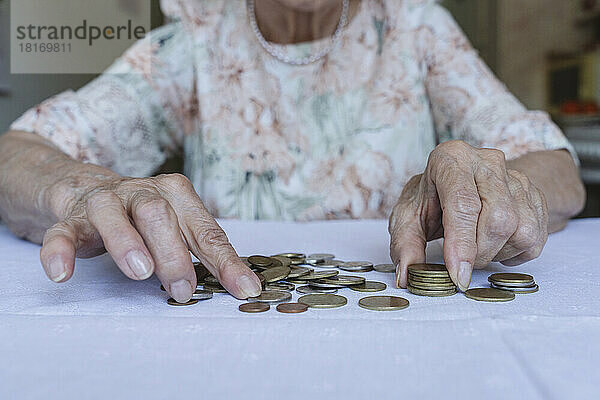 Senior woman stacking coins on table at home