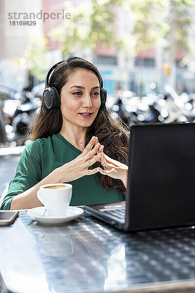 Freiberufler mit Kopfhörern und Laptop im Straßencafé