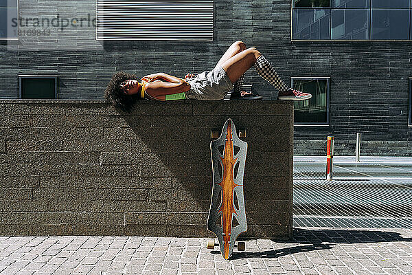 Frau liegt an sonnigem Tag mit Skateboard auf Wand
