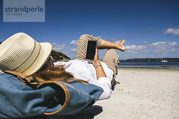 Reife Frau entspannt sich und nutzt ihr Smartphone am Strand