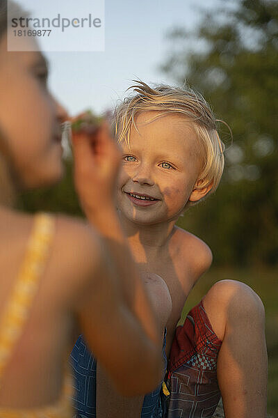 Lächelnder Junge  der die riechende Blume seiner Schwester anschaut