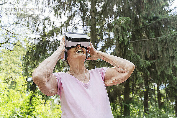 Ältere Frau schaut durch VR-Brille zu und lacht im öffentlichen Park